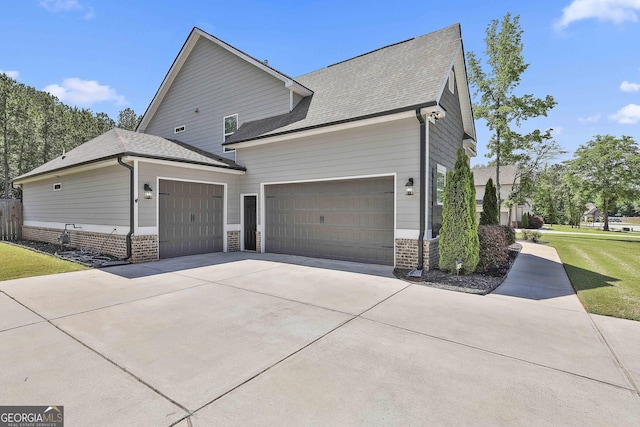 view of side of property featuring an attached garage, brick siding, concrete driveway, roof with shingles, and a yard