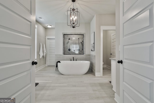 full bath featuring a tile shower, a chandelier, a soaking tub, wood finished floors, and baseboards