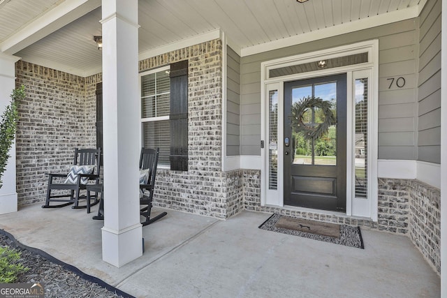 view of exterior entry featuring brick siding and covered porch