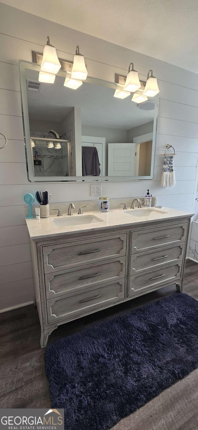 bathroom with double vanity, wood walls, wood finished floors, and a shower with door