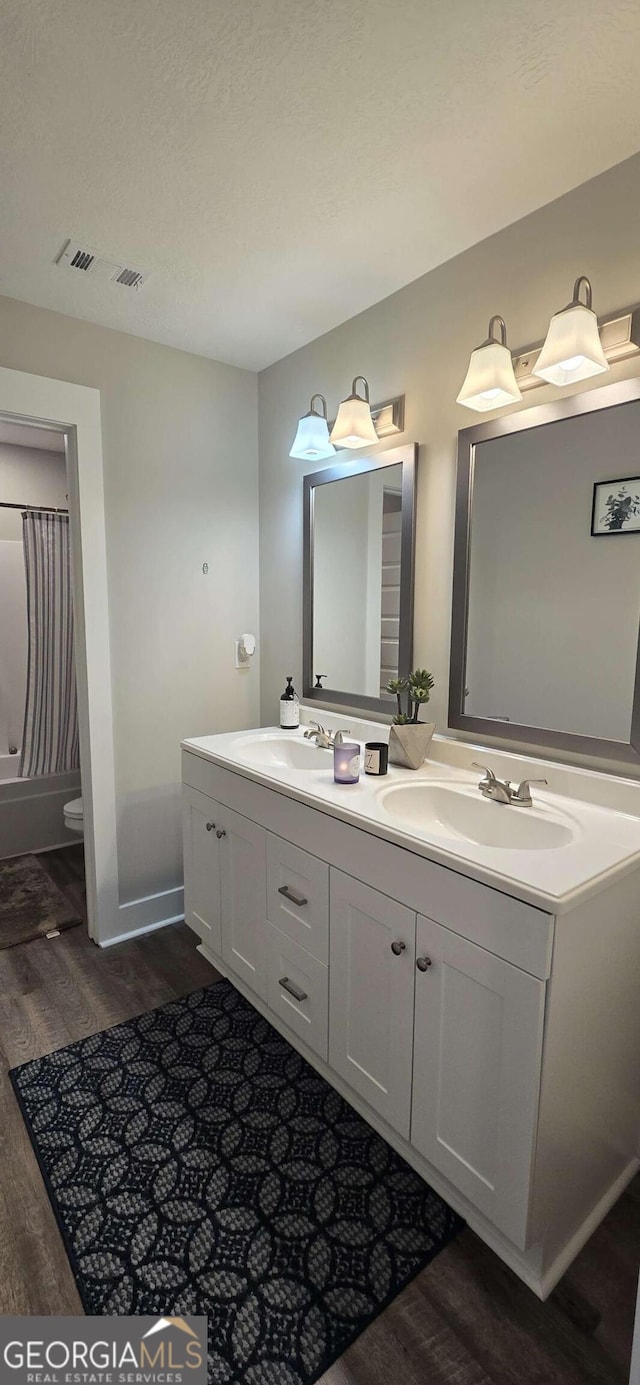 full bathroom featuring wood finished floors, double vanity, toilet, baseboards, and shower / bath combo