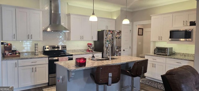 kitchen with wall chimney range hood, stainless steel appliances, tasteful backsplash, a kitchen island with sink, and white cabinetry