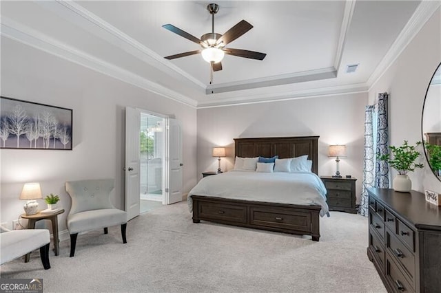 bedroom with a raised ceiling, light colored carpet, ornamental molding, ensuite bath, and a ceiling fan