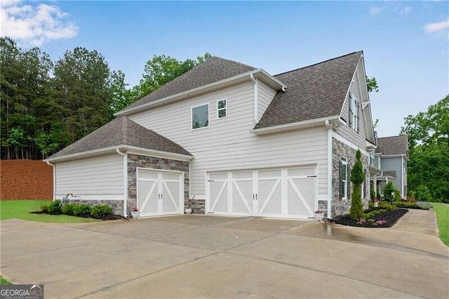 view of side of property featuring stone siding, concrete driveway, roof with shingles, and an attached garage