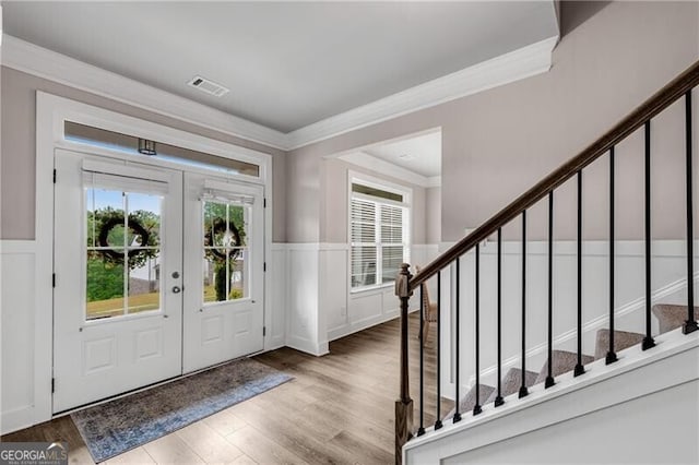 foyer featuring stairs, a wainscoted wall, wood finished floors, crown molding, and french doors