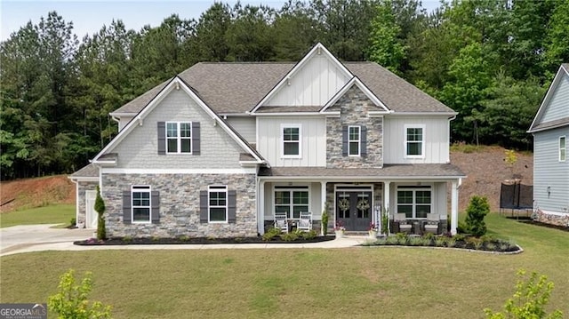 craftsman-style home featuring board and batten siding, a trampoline, a front yard, covered porch, and stone siding