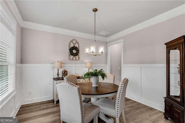 dining room featuring a chandelier, a decorative wall, wainscoting, ornamental molding, and light wood-type flooring