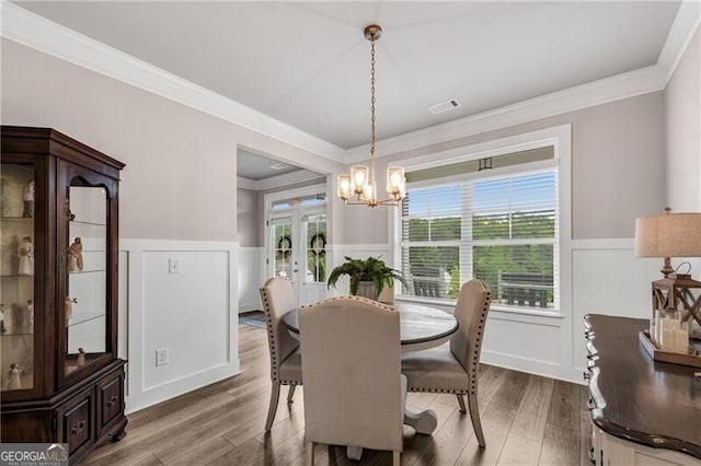 dining area with wainscoting, a decorative wall, ornamental molding, wood finished floors, and a chandelier