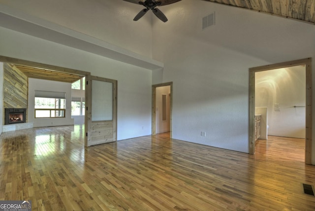 unfurnished living room featuring a ceiling fan, wood finished floors, a stone fireplace, and a high ceiling