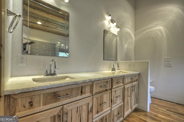 bathroom featuring wood finished floors, double vanity, toilet, a textured wall, and a shower