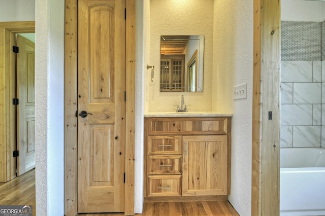 bathroom featuring a textured wall, wood finished floors, a bath, and vanity