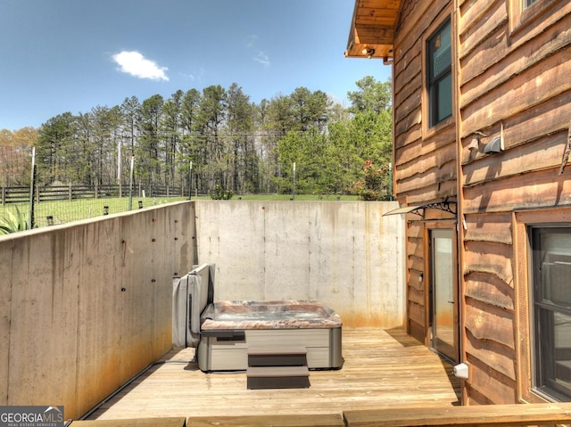 view of patio / terrace with fence, a hot tub, view of wooded area, and a deck