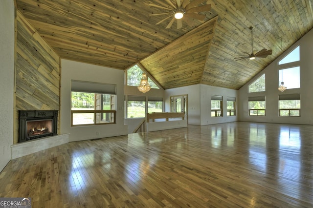 unfurnished living room featuring ceiling fan, high vaulted ceiling, a warm lit fireplace, wood-type flooring, and wood ceiling