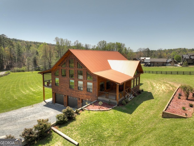 rear view of house featuring covered porch, an attached garage, gravel driveway, and a wooded view