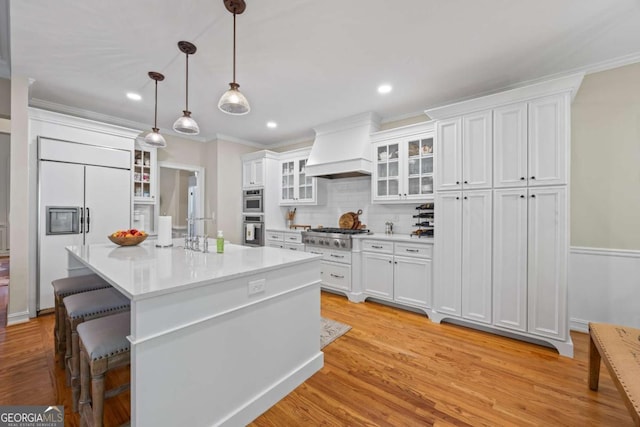 kitchen featuring custom exhaust hood, stainless steel appliances, a kitchen bar, light countertops, and white cabinetry