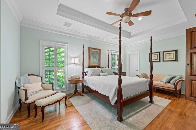bedroom featuring a tray ceiling, light wood-style flooring, crown molding, a ceiling fan, and baseboards