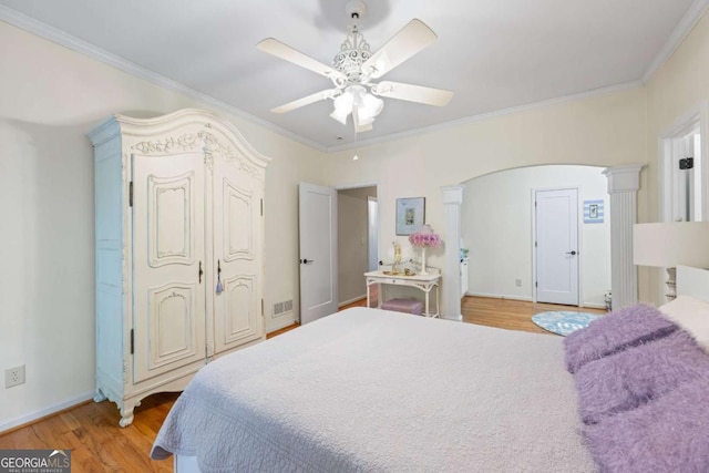bedroom featuring crown molding, light wood-type flooring, baseboards, a ceiling fan, and decorative columns