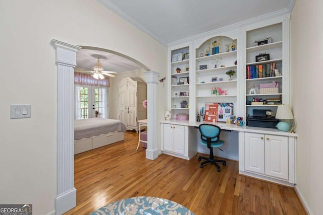 office area with ornate columns, arched walkways, light wood-style floors, built in study area, and ornamental molding