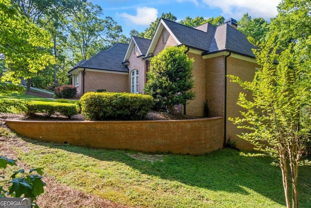 view of home's exterior with a yard, brick siding, and a chimney