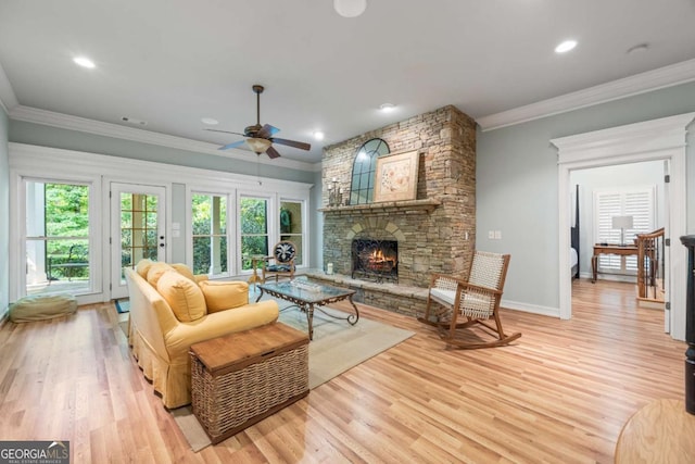 living area featuring a fireplace, ceiling fan, light wood finished floors, crown molding, and baseboards