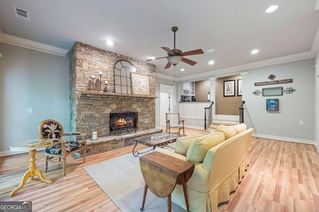 living area featuring a ceiling fan, crown molding, a stone fireplace, light wood-style flooring, and recessed lighting