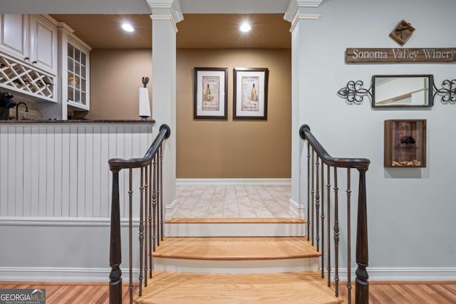 stairway featuring bar area, wood finished floors, baseboards, recessed lighting, and ornate columns