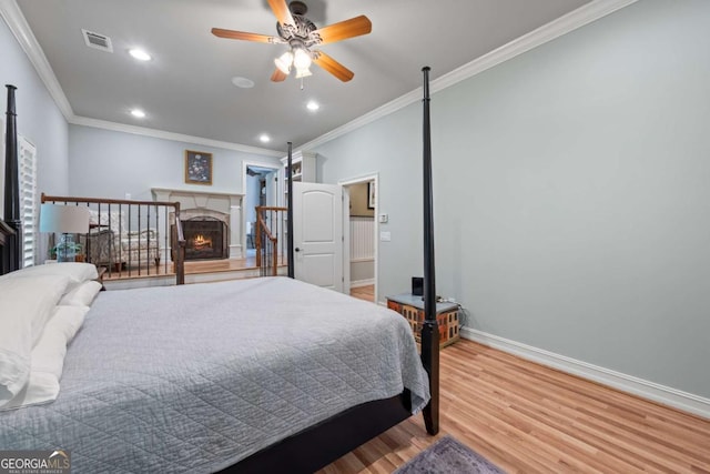 bedroom with crown molding, wood finished floors, baseboards, a warm lit fireplace, and recessed lighting