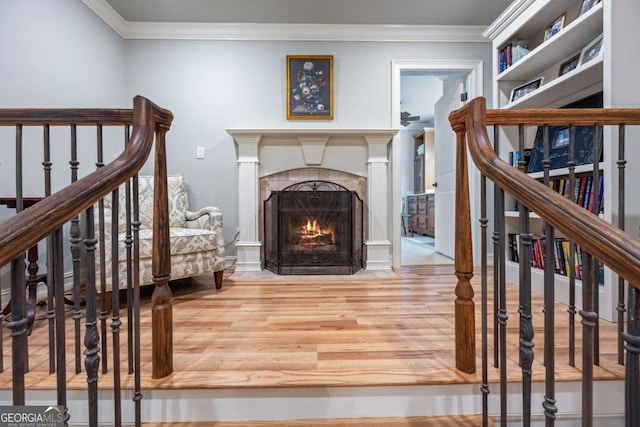 living area with wood finished floors, ornamental molding, a fireplace with flush hearth, and stairs