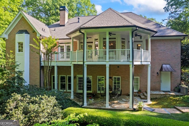 rear view of property with a ceiling fan, a chimney, a balcony, and brick siding