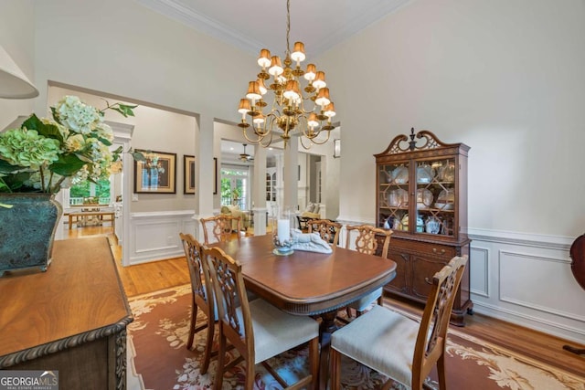 dining room with light wood-style floors, crown molding, a chandelier, a wainscoted wall, and a decorative wall