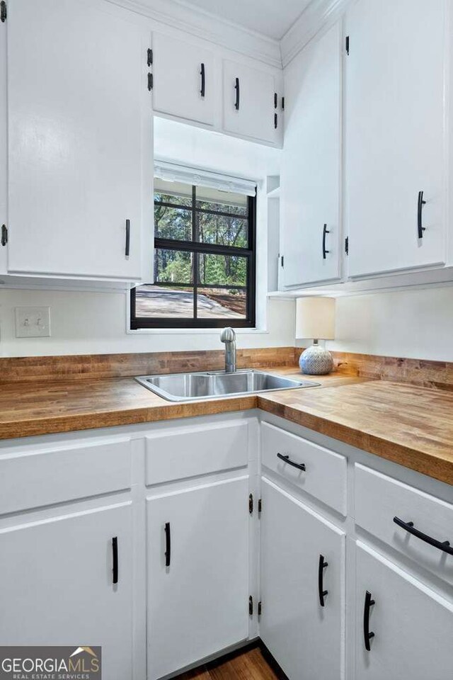 kitchen featuring butcher block countertops, a sink, white cabinets, and ornamental molding