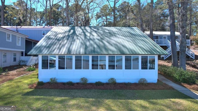 view of side of property with a lawn, a sunroom, and metal roof