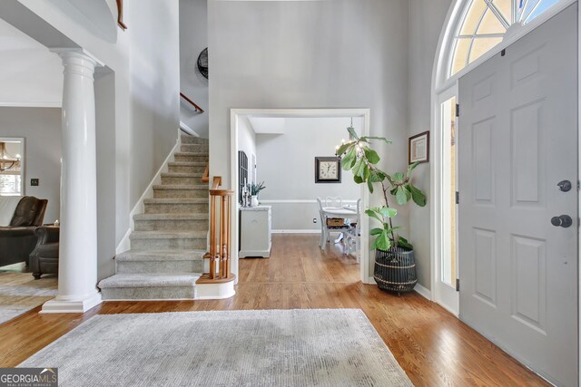 entryway with decorative columns, stairway, a towering ceiling, wood finished floors, and baseboards
