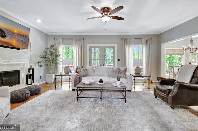 living room with plenty of natural light, a ceiling fan, wood finished floors, a fireplace with raised hearth, and ornamental molding