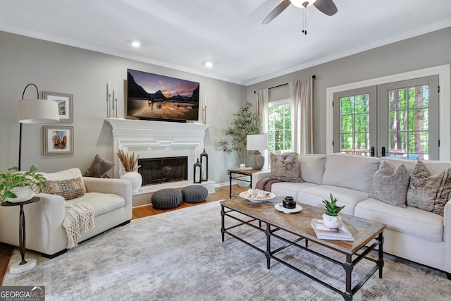 living room featuring french doors, ceiling fan, wood finished floors, crown molding, and a fireplace with raised hearth