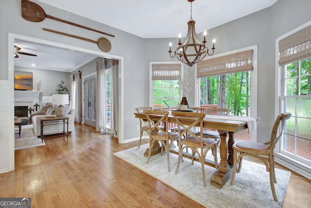 dining space with a chandelier, light wood-type flooring, baseboards, ceiling fan, and a fireplace