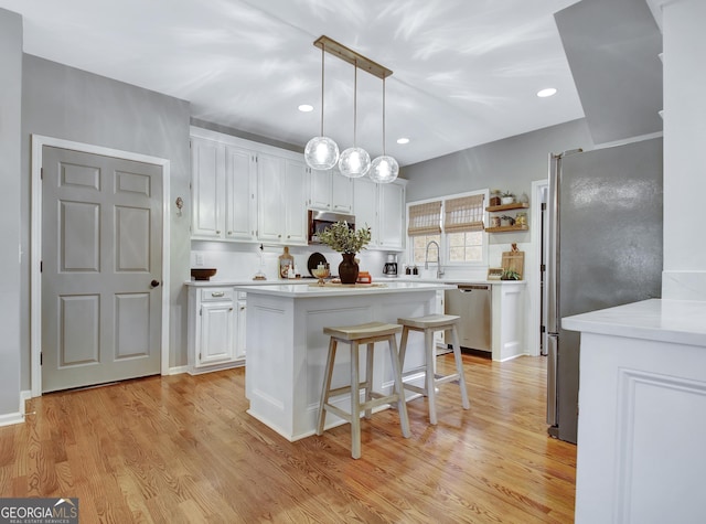 kitchen featuring appliances with stainless steel finishes, white cabinetry, a center island, light countertops, and light wood-style floors