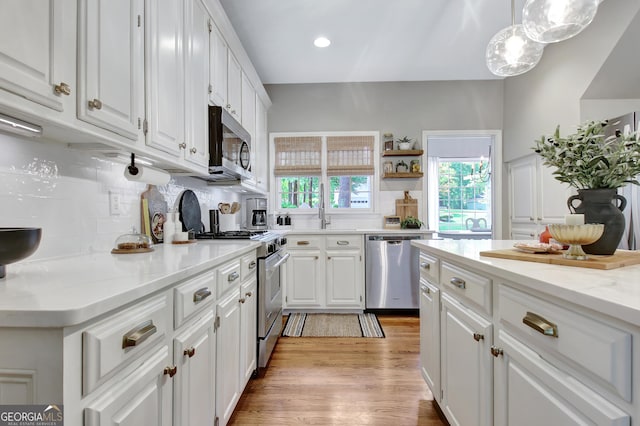 kitchen featuring appliances with stainless steel finishes, white cabinetry, decorative backsplash, light wood-style floors, and a sink