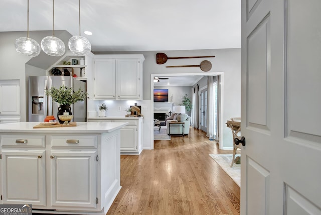 kitchen with stainless steel refrigerator with ice dispenser, light wood-type flooring, light countertops, white cabinets, and vaulted ceiling