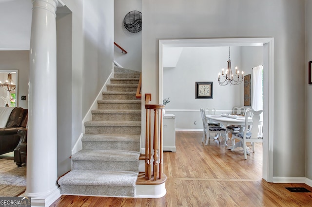 stairs with wood finished floors, a chandelier, baseboards, and ornate columns