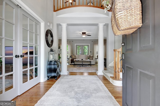 entryway featuring ornate columns, crown molding, ceiling fan, a towering ceiling, and wood finished floors