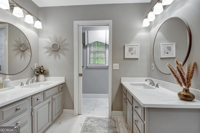 bathroom with marble finish flooring, baseboards, and two vanities
