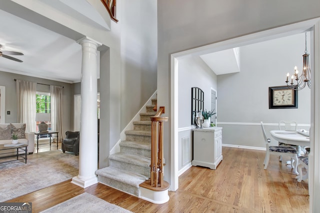 stairway featuring wood finished floors, ceiling fan, decorative columns, baseboards, and a chandelier