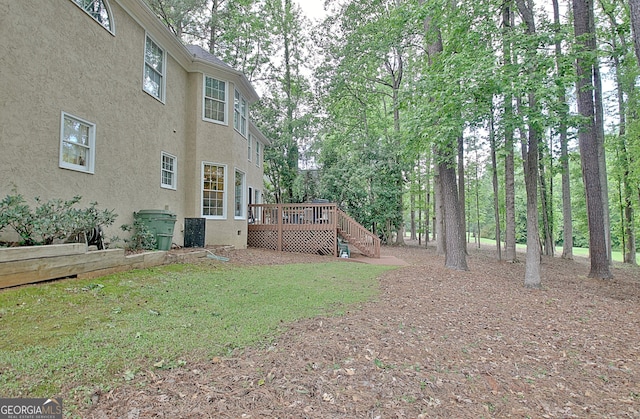 view of green lawn featuring a wooden deck, stairs, and view of wooded area