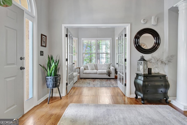 foyer entrance featuring french doors, decorative columns, wood finished floors, and baseboards