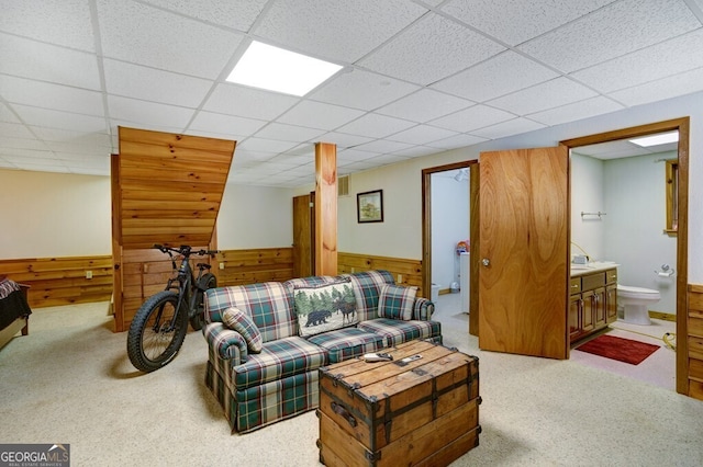 living room with wood walls, a drop ceiling, a wainscoted wall, and carpet