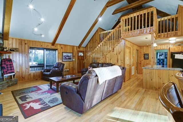 living area with beam ceiling, high vaulted ceiling, stairs, wooden walls, and wood finished floors