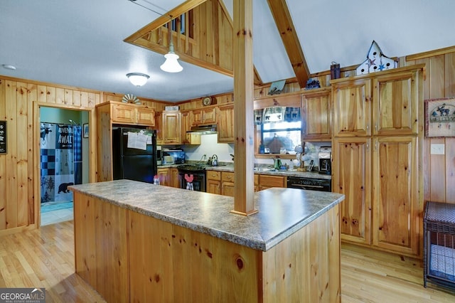 kitchen featuring black appliances, light wood-style floors, wooden walls, under cabinet range hood, and pendant lighting