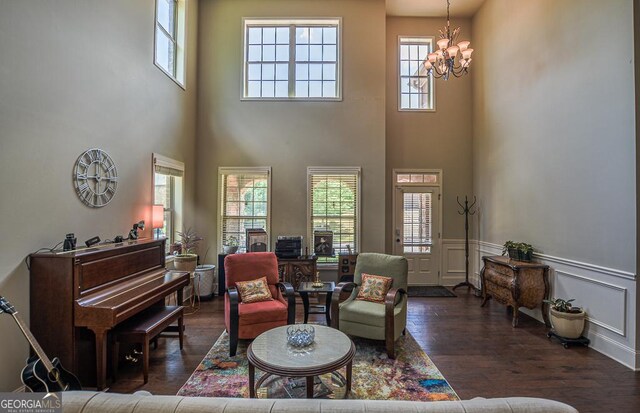 living area featuring a chandelier, dark wood finished floors, healthy amount of natural light, a high ceiling, and wainscoting