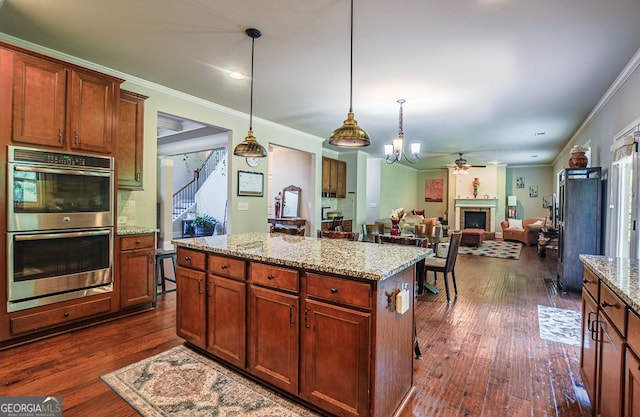 kitchen with stainless steel double oven, ceiling fan, dark wood-type flooring, a fireplace, and crown molding